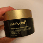 Hand holding Medicube Deep Vita C Capsule Cream vitamin C moisturizer in a dark amber jar with a gold lid.