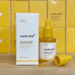 Medicube Kojic Acid Turmeric Niacinamide Serum 30ml yellow dropper bottle with glass pipette displayed next to its white product box on a wooden surface with yellow packaging background.
