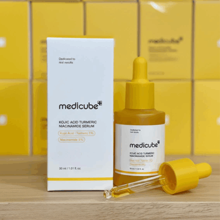 Medicube Kojic Acid Turmeric Niacinamide Serum 30ml yellow dropper bottle with glass pipette displayed next to its white product box on a wooden surface with yellow packaging background.
