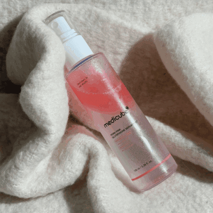 Medicube PDRN Pink Glutathione Serum Mist 100ml bottle with pink gradient liquid placed on soft white fabric background.