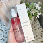 Hand holding Medicube PDRN Pink Glutathione Serum Mist 100ml bottle next to its white box packaging with flowers in the background.
