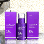 Medicube Retinol NMN Boosting Serum 1.9% bottle displayed between two purple product boxes on a glass surface.
