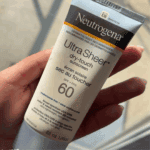 Hand holding Neutrogena Ultra Sheer Dry-Touch Sunscreen SPF 60 88ml tube in natural sunlight