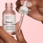 A close-up of hands holding The Ordinary Hyaluronic Acid 2% + B5 serum bottle and dropper, dispensing a clear hydrating serum onto the skin, highlighting its lightweight texture and moisturizing properties.