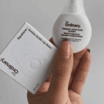 Hand holding The Ordinary Squalane + Amino Acids Lip Balm 15ml with product box